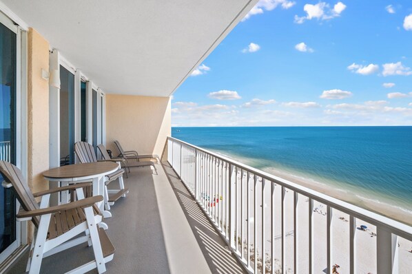 A balcony with a view of the ocean, white railings, and outdoor seating.