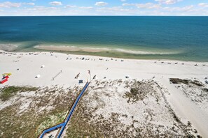 An aerial view of a beach with a sandy shore, clear blue water, and a few people and umbrellas.