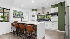 A modern kitchen with a central island, bar stools, and a view of greenery outside.