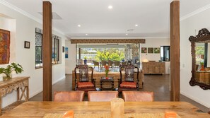 A dining area with a wooden table and chairs, a view of the outdoors, and a stone fireplace. - The Doggy Beach House -  with Pool in Pottsville (Pottsville)