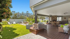 Relax by the fireplace in this serene outdoor space, surrounded by lush greenery and a beautiful view.