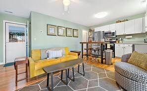 A compact living space with a yellow sofa, a patterned sofa, a dining table, and a kitchenette.