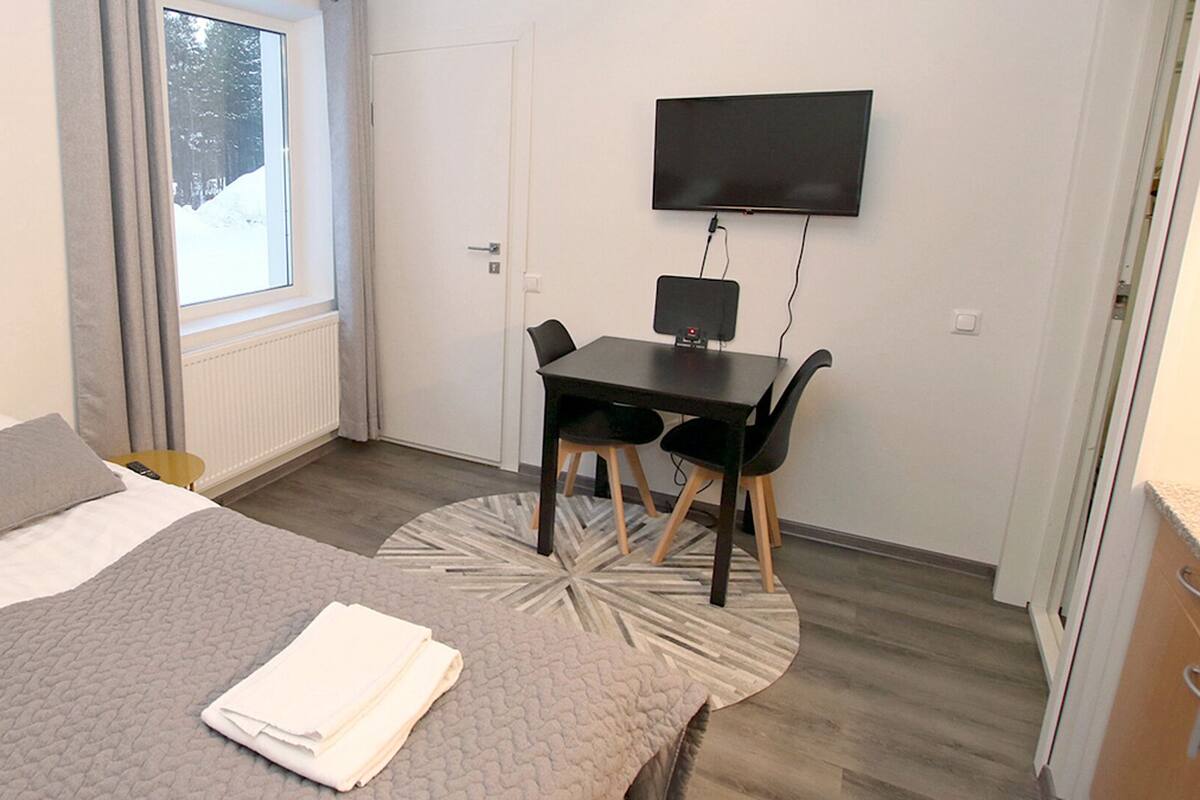 A bedroom with a bed, a desk, and a chair. There is a TV mounted on the wall.