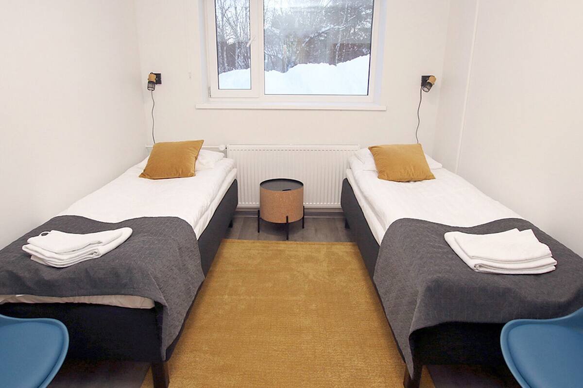 A small, clean room with two single beds, a small round table, and a window with a view of a snowy landscape.