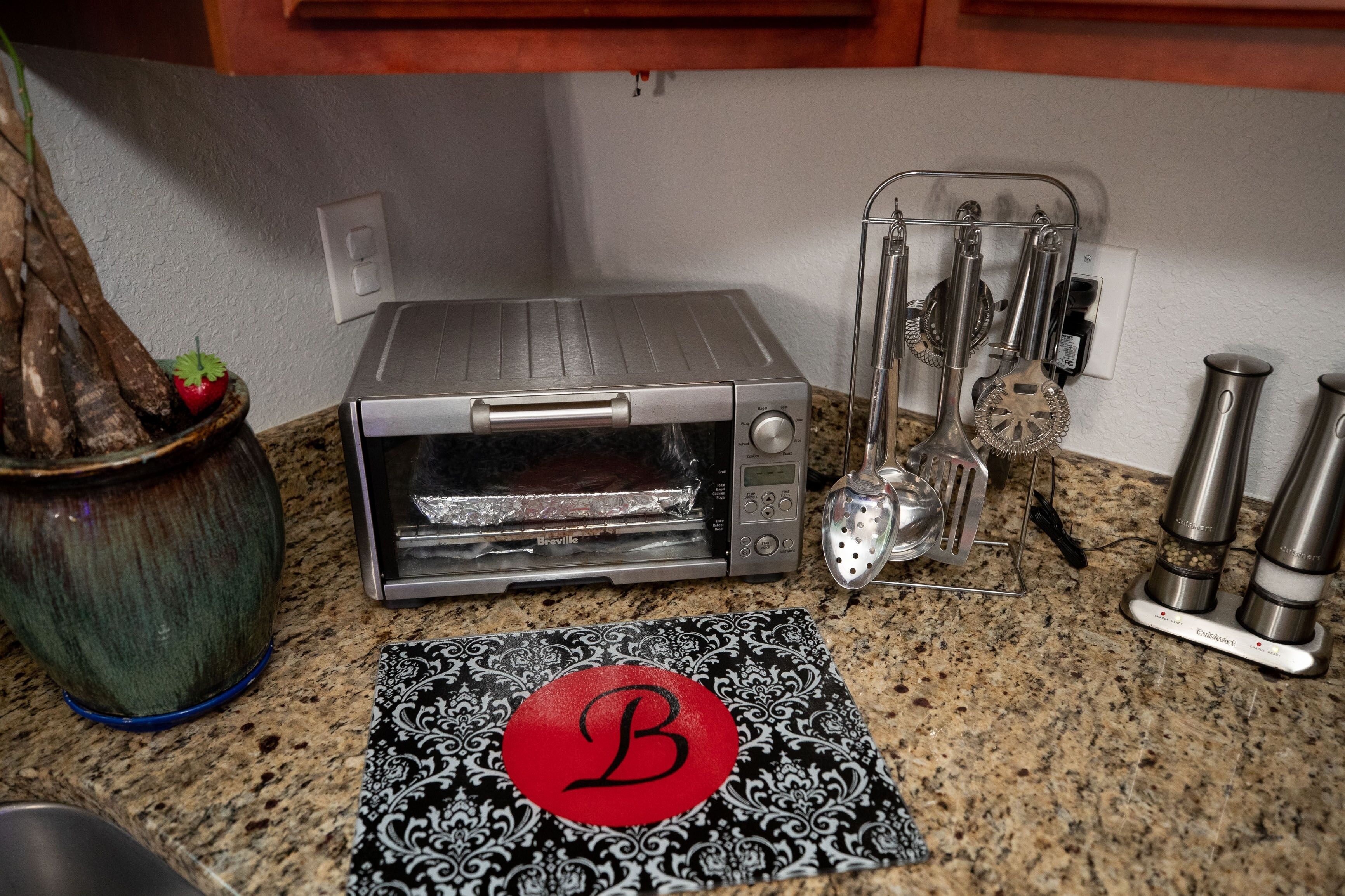 A kitchen with a toaster oven, a spice rack, and a decorative mat with a letter 'B'.