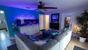 Un salon moderne avec un canapé blanc, un ventilateur de plafond, un grand aquarium et un téléviseur.