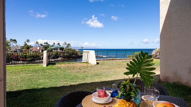 A table with tropical fruits and a drink, overlooking a beach with a clear sky. - Napili Point B33 1 Bedroom Oceanfront Condo 1 Condo by RedAwning (Lahaina)