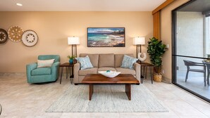 A living room with a beige sofa, teal armchair, wooden coffee table, and a large window offering a view of the outdoors. - Napili Point B33 1 Bedroom Oceanfront Condo 1 Condo by RedAwning (Lahaina)