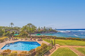 A pool area with lounge chairs and a view of the ocean.