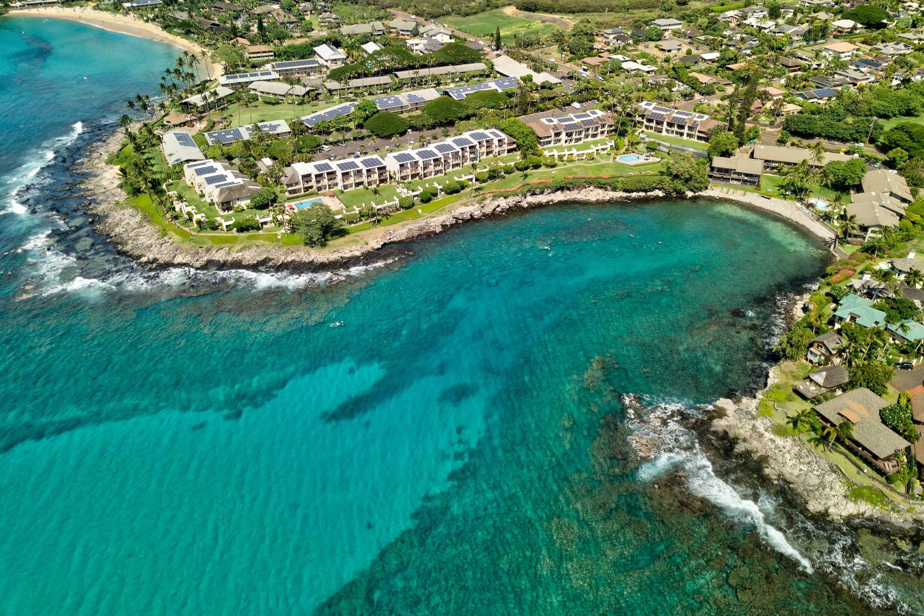 An aerial view of a coastal resort with multiple buildings, a beachfront, and clear turquoise waters.