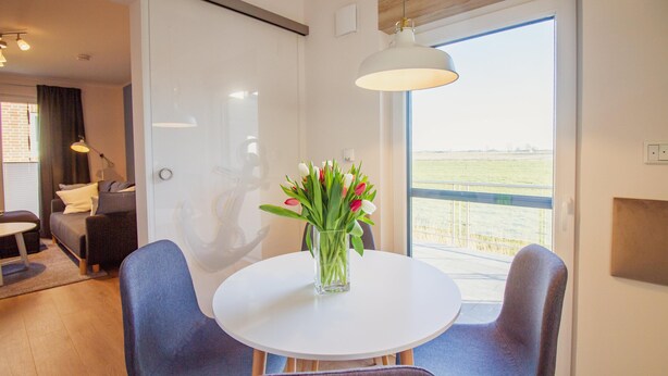 Un comedor moderno con una mesa redonda blanca, dos sillas azules y un jarrón con flores.
