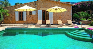 Ein Steinhaus mit Pool, Sonnenschirmen und Liegestühlen.