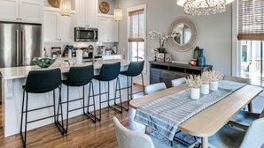 A modern kitchen with white cabinets, stainless steel appliances, and a central island with bar stools. - Carlton Landing-True Blue (Carlton Landing)