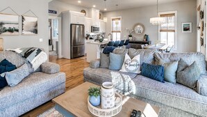 A spacious living area with a large gray sofa, a coffee table with decorative items, and a kitchen in the background. - Carlton Landing-True Blue (Carlton Landing)