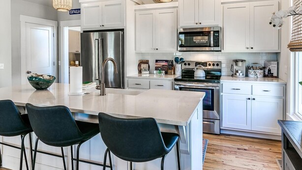 A modern kitchen with white cabinets, stainless steel appliances, and a central island with bar stools. - Carlton Landing-True Blue (Carlton Landing)