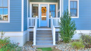 A blue house with a front porch, a wreath on the door, and a small garden with rocks and plants. - Carlton Landing-True Blue (Carlton Landing)