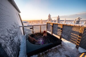 A snow-covered outdoor hot tub area with a view of a snowy landscape and trees.