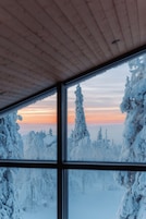 A room with a large window overlooking a snowy landscape at sunset.