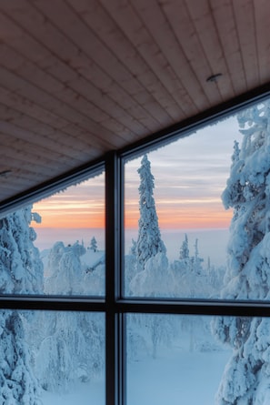 Una habitación con un amplio ventanal con vistas a un paisaje nevado al atardecer.