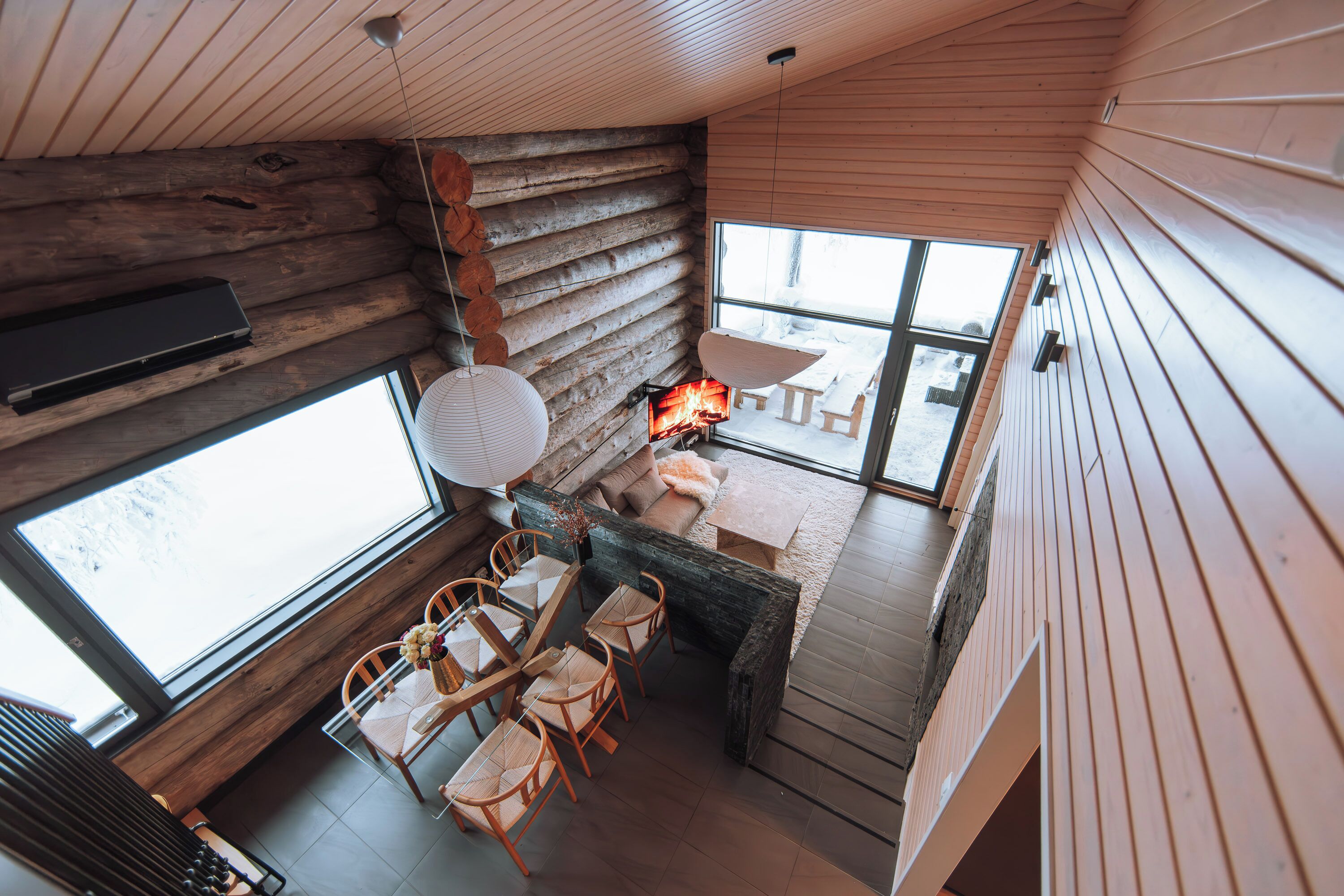 Un intérieur de chalet chaleureux avec une cheminée, des meubles en bois et de grandes fenêtres.