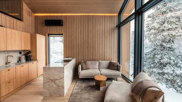 Un intérieur moderne avec un lambris en bois, un coin cuisine, un canapé et une grande fenêtre donnant sur un paysage enneigé.