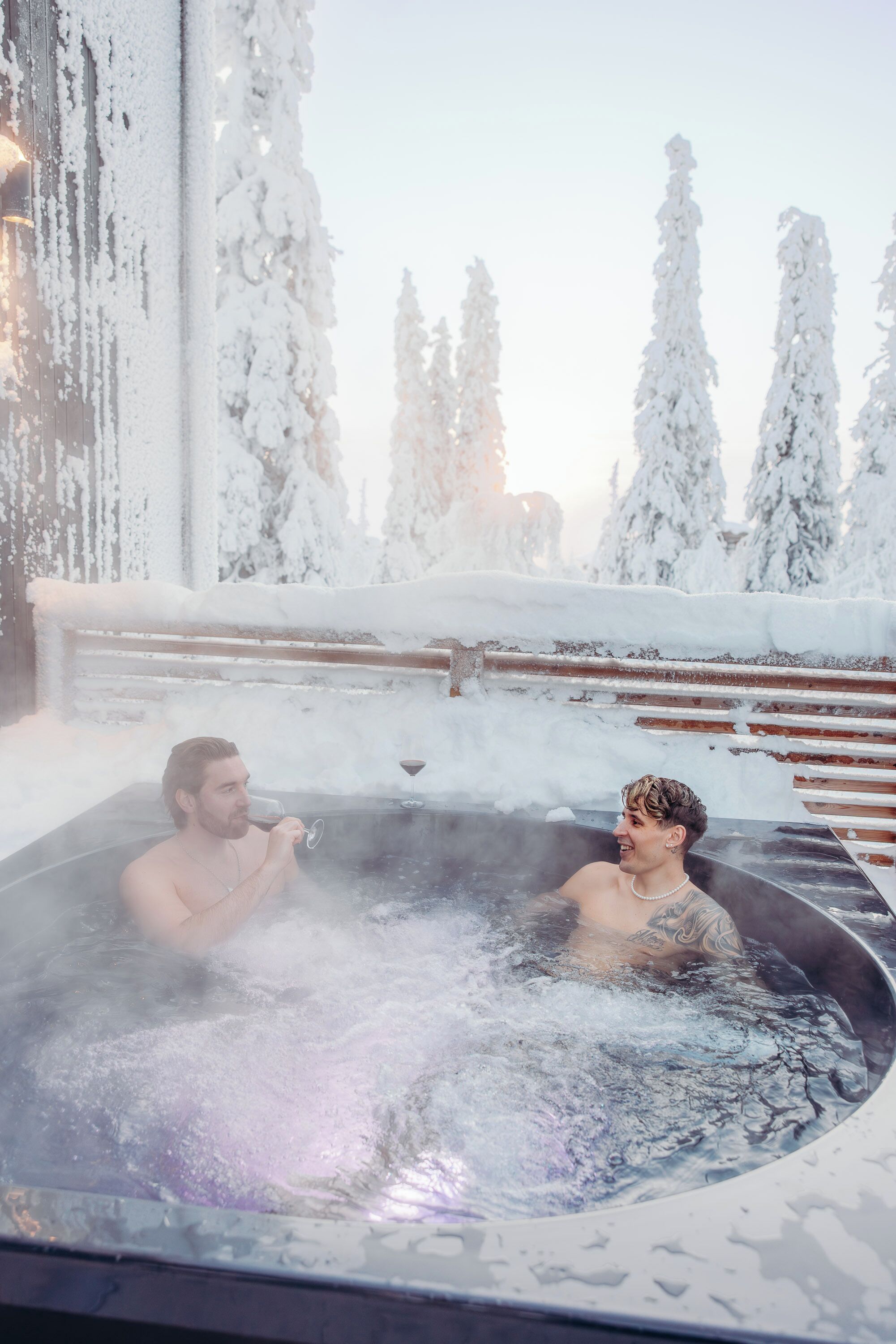Two individuals in a hot tub surrounded by snow-covered trees.