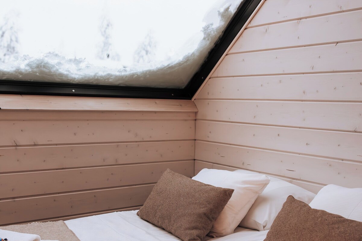 Une chambre confortable avec un plafond en pente et un puits de lumière, comprenant deux lits avec des oreillers et des serviettes pliées.