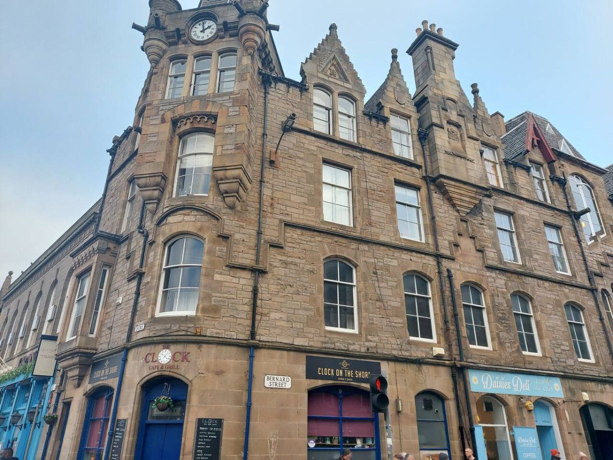 A historic building with multiple commercial establishments on the ground floor, including a clock, cafe, and deli.