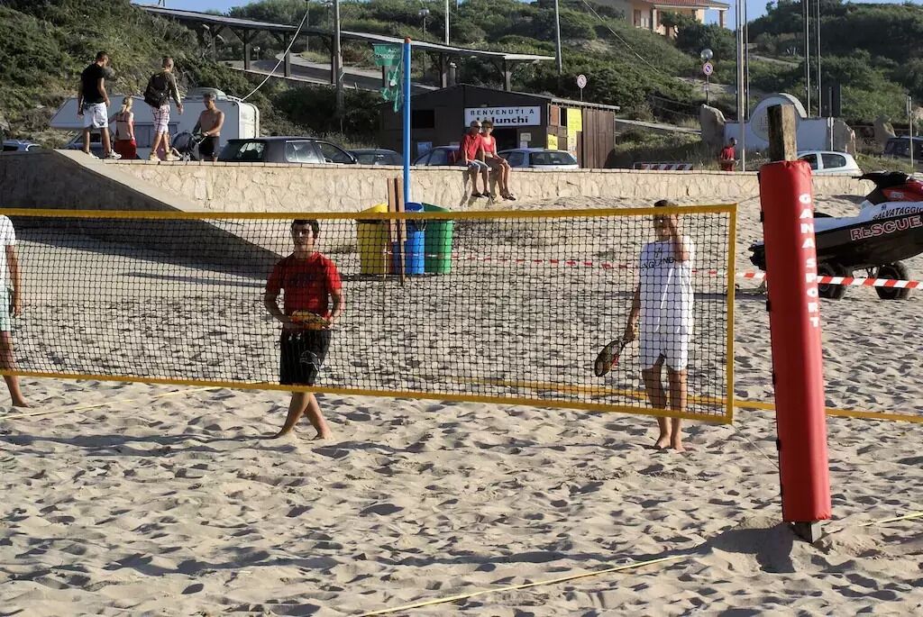 Una cancha de voleibol de playa con red, arena y gente.