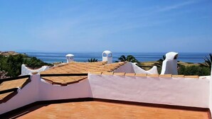 A rooftop terrace with a view of the sea, white walls, and terracotta tiles.