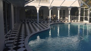 A swimming pool with a checkered floor, surrounded by covered seating areas and large windows. - Villa Camellia 5bed/4.5 bath with private pool and golf course view (Lehigh Acres)