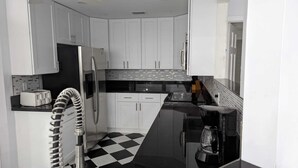 A compact kitchen with white cabinets, a black and white checkered floor, a toaster, a refrigerator, a coffee maker, and a sink. - Villa Camellia 5bed/4.5 bath with private pool and golf course view (Lehigh Acres)