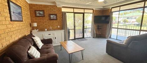 A living room with a brick wall, a sofa, a coffee table, a TV, and a sliding glass door leading to an outdoor area.