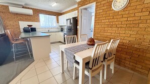 A kitchen with a dining area, white cabinets, a refrigerator, and a clock on the wall.