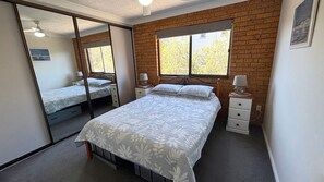 A bedroom with a large bed, two bedside tables, a mirror, and a window with a view of trees.