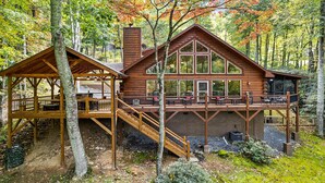 Een chalet met terras, een overdekte zithoek en een groot raam met uitzicht op het bos.