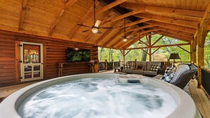 Een houten chalet met een jacuzzi, een televisie en een gezellige zithoek met uitzicht op bomen.