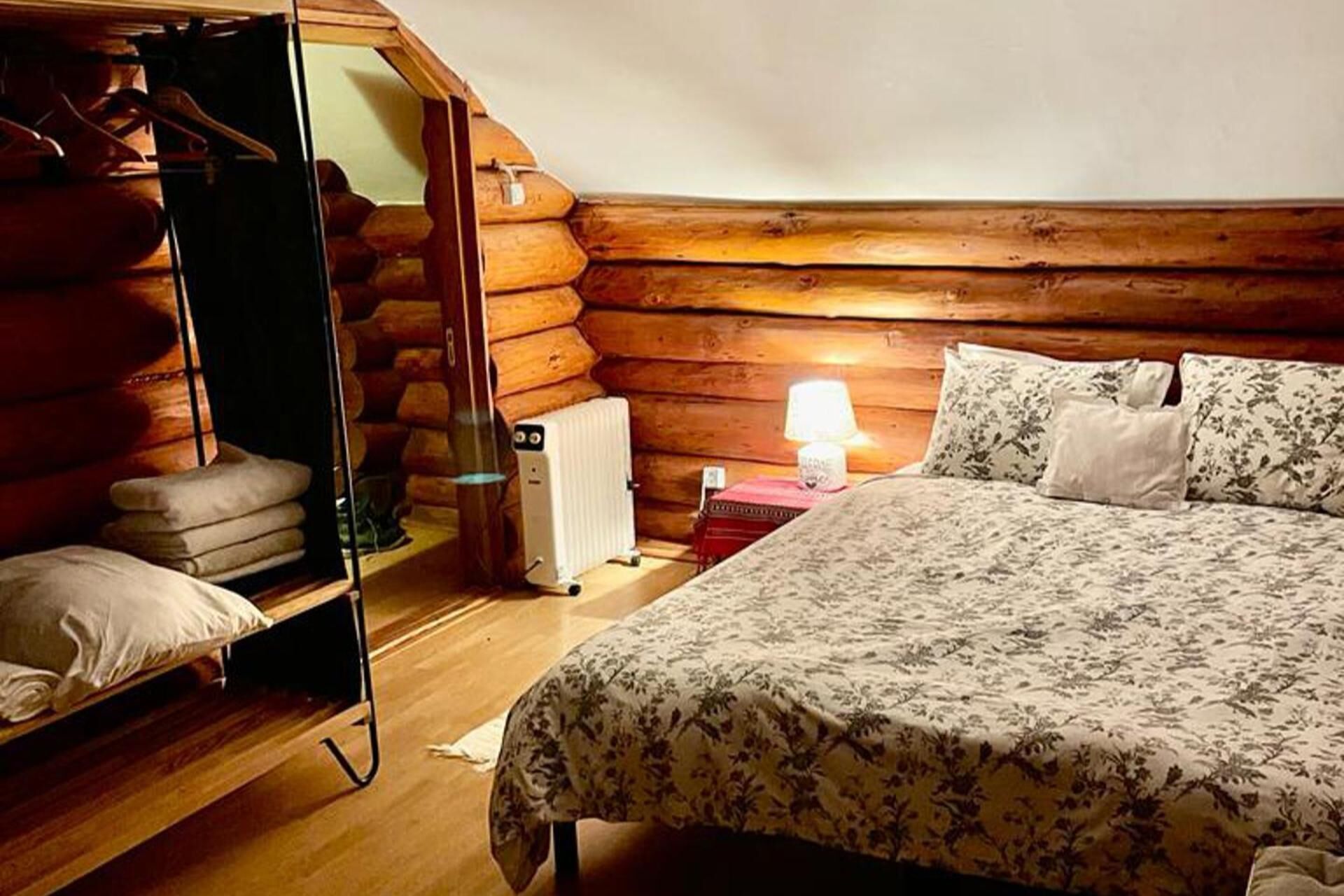A log cabin room with a bed, a wooden wardrobe, and a radiator.