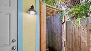A wooden door with a metal handle, a light fixture above it, and a wooden fence with a woven roof. - Sand and Sea 109 A! Pool, Patio and Coastal Charm! (Anna Maria)