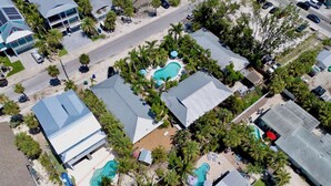 An aerial view of a residential area with multiple houses, a swimming pool, and a road. - Quaint Condo with Shared Pool, Only 2 Houses to the Beach - Sand And Sea 109 B (Anna Maria)