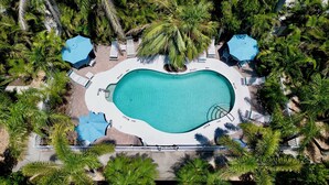 An aerial view of a swimming pool surrounded by palm trees and sun loungers. - Quaint Condo with Shared Pool, Only 2 Houses to the Beach - Sand And Sea 109 B (Anna Maria)