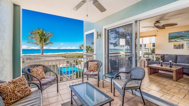 A balcony with wicker furniture, a glass table, and a view of the ocean.