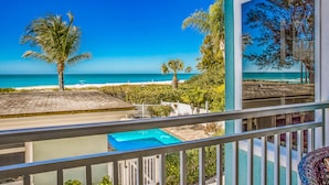 A balcony with a view of a swimming pool, a beach, and a tropical landscape.
