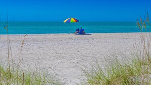 A beach scene with a colorful umbrella and two people sitting on the sand.