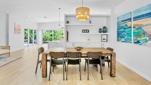 A modern dining area with a wooden table and chairs, a hanging light fixture, and artwork on the walls.