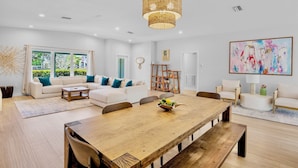 A spacious living room with a large wooden dining table, white sofas, and a hanging rattan light fixture.