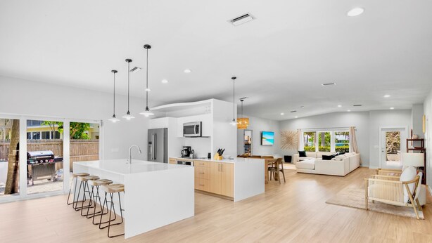 A modern kitchen with a central island, bar stools, and a dining area with a sofa and table.