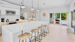 A modern kitchen with a large island, bar stools, and a view of a pool.