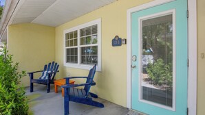 A yellow house with a blue door, two blue Adirondack chairs, and a small table. - Steps to Beach and Pool! Cozy Island Flat Near Pine Ave! (Anna Maria)