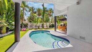 A modern outdoor swimming pool with a clear blue water feature, surrounded by lush greenery and a white wall structure. - Luxury home near the beach and shopping! Private backyard and pool! (Anna Maria)